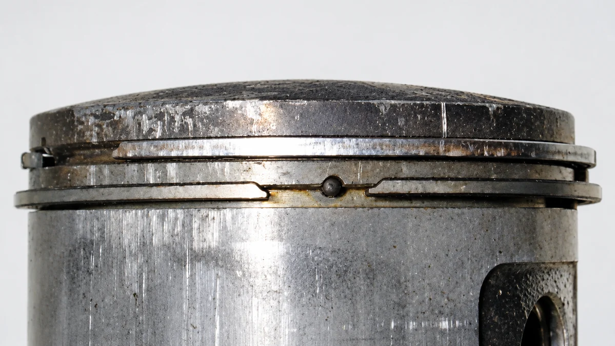 Primer plano de dos anillos en un pistón usado, con las puntas de los anillos y las marcas de la superficie visibles sobre un fondo neutro claro